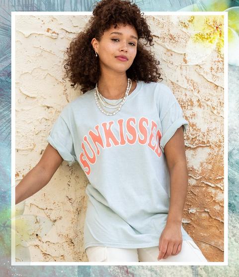 Woman wearing a light blue garment wash graphic tee that reads "Sunkissed"
