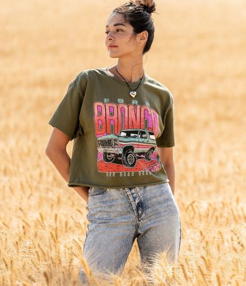 Woman wearing a forest green 1979 broncos cropped graphic tee with light wash blue jeans.