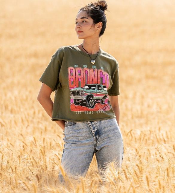 Woman wearing a forest green 1979 broncos cropped graphic tee with light wash blue jeans.