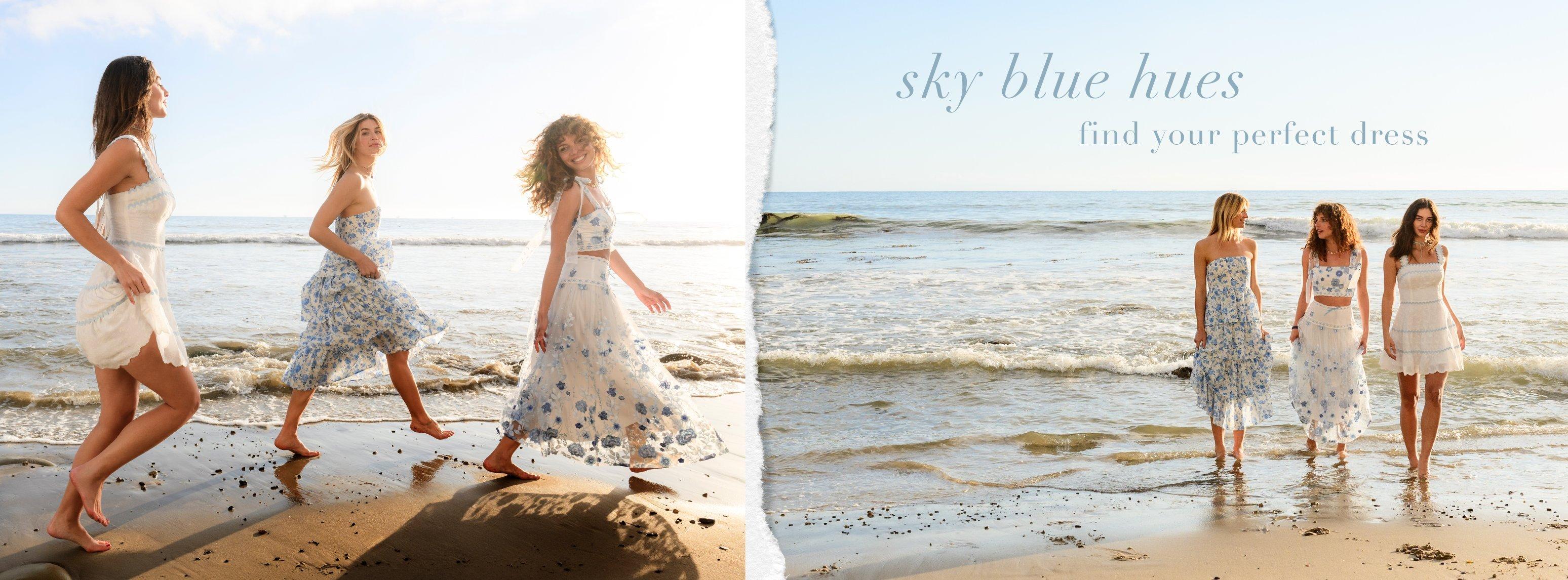 Three girls running on the beach in blue and white dresses