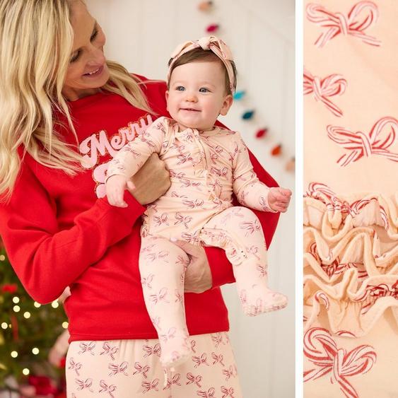 Baby girl wearing a candy cane bow onesie being held by a woman with matching pajamas.