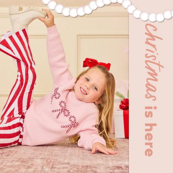 little girl wearing red and white striped pants and a candy cane bow sweater