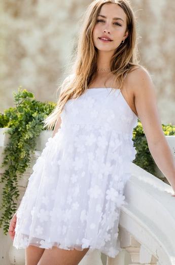 Woman wearing a white babydoll mini dress with 3D floral appliques and spaghetti straps