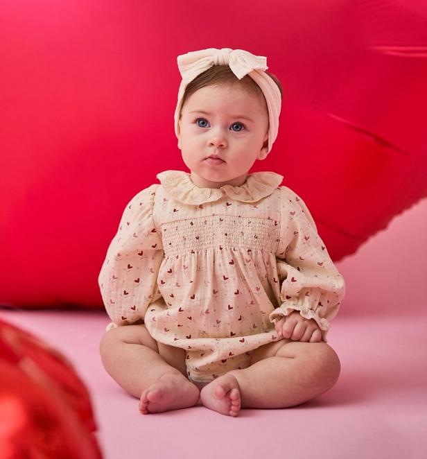 Baby girl wearing a heart onesie with a headband.