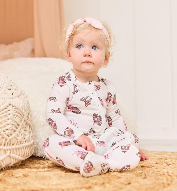 Little girl wearing a football and bows themed onesie