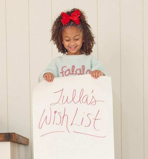 little girl wearing a teal sweater holding a wishlist.