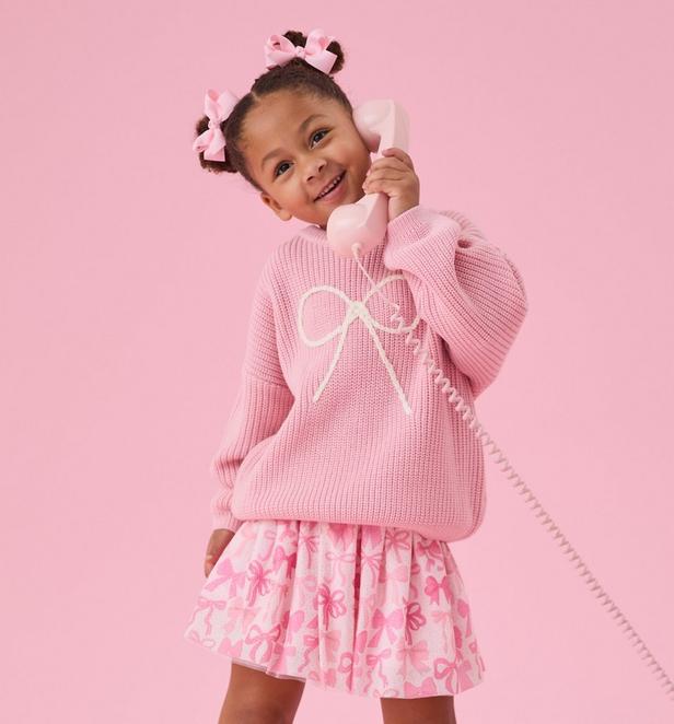 Little girl wearing pink skirt and bow sweater.