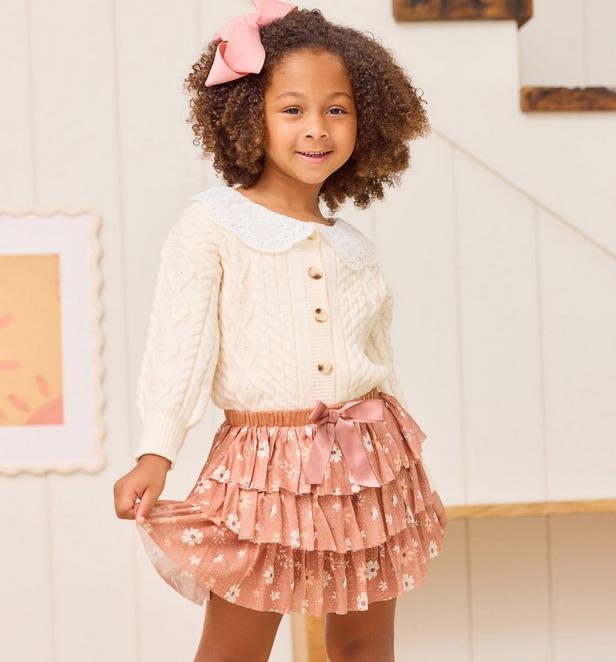 Little girl wearing a pink layered floral skirt and cream cardigan