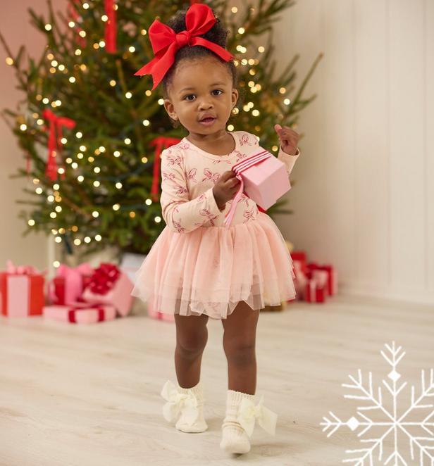 Little girl wearing pink bow candy cane dress, and a red bow headband.