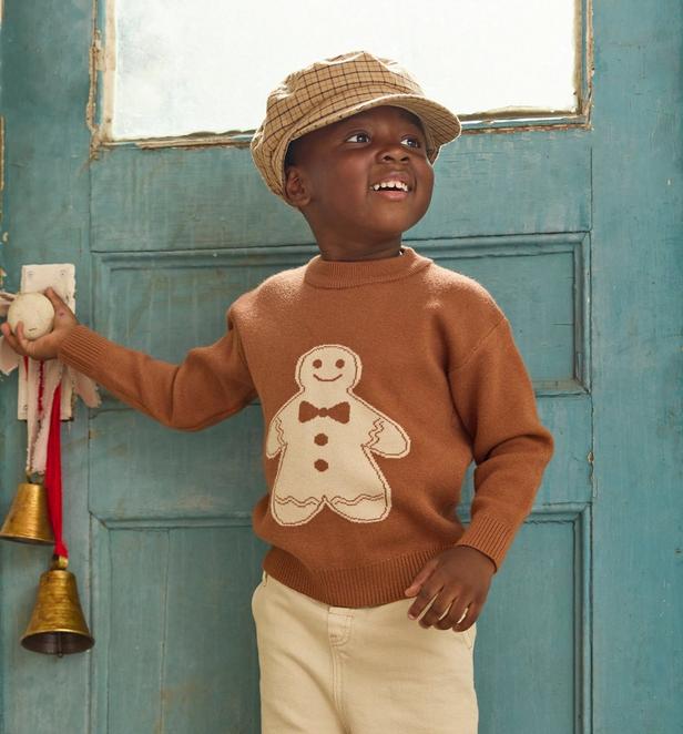 Little boy wearing tan gingerbread sweater and a plaid hat.