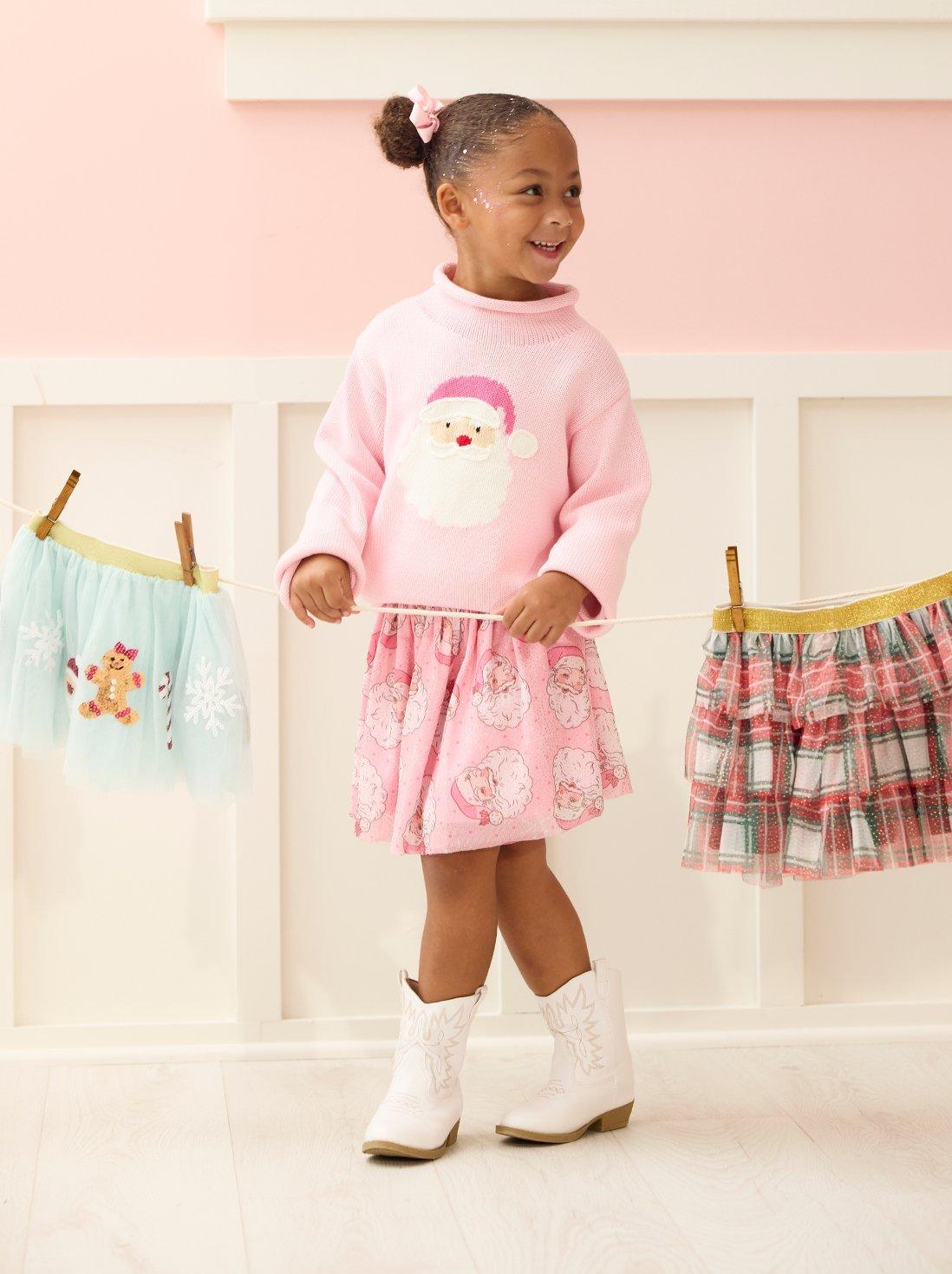 Little girl wearing a pink toto and holding a rope with various other colored tutus.