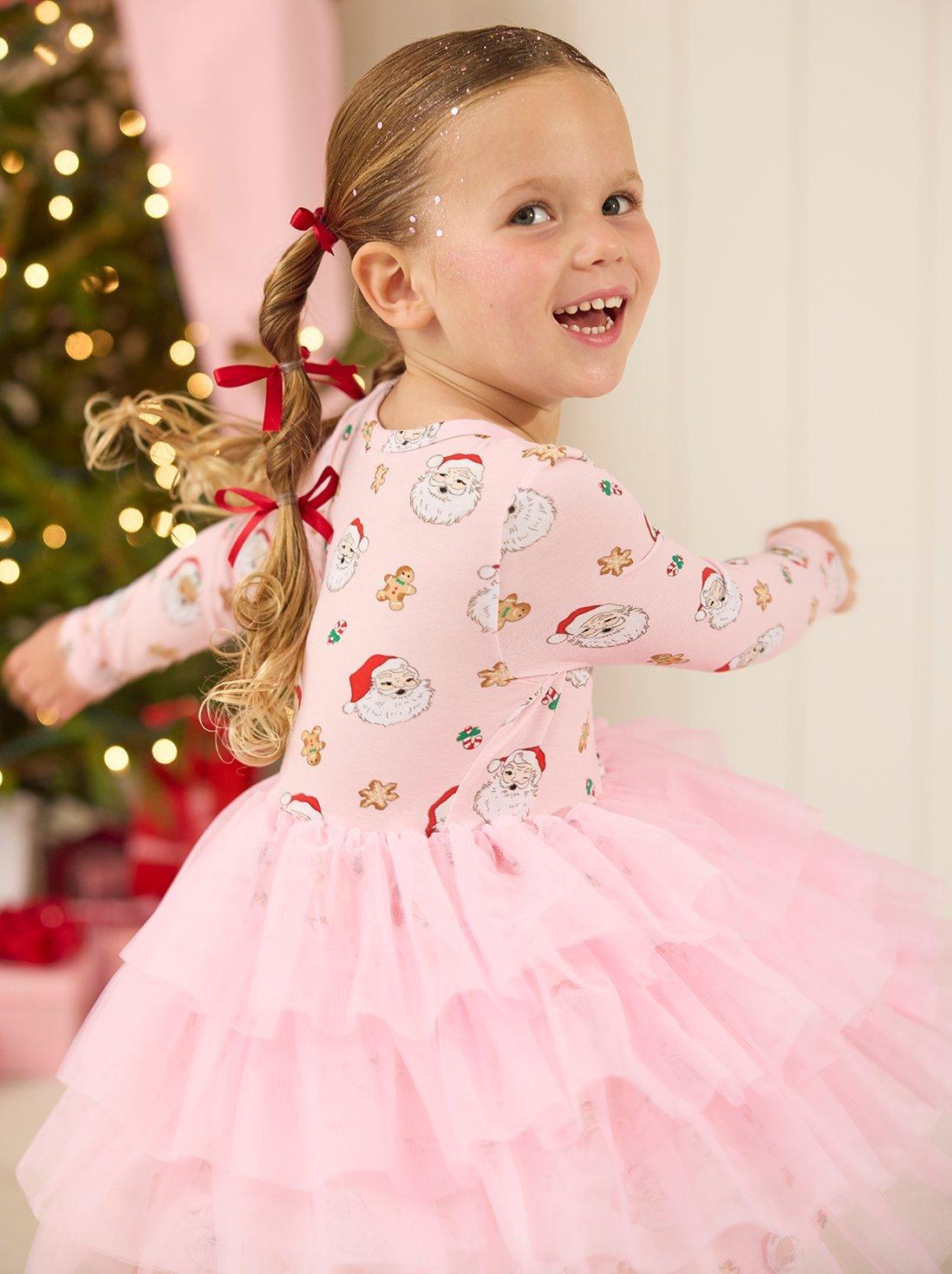 Young girl wearing a pink christmas dress with santa pattern.