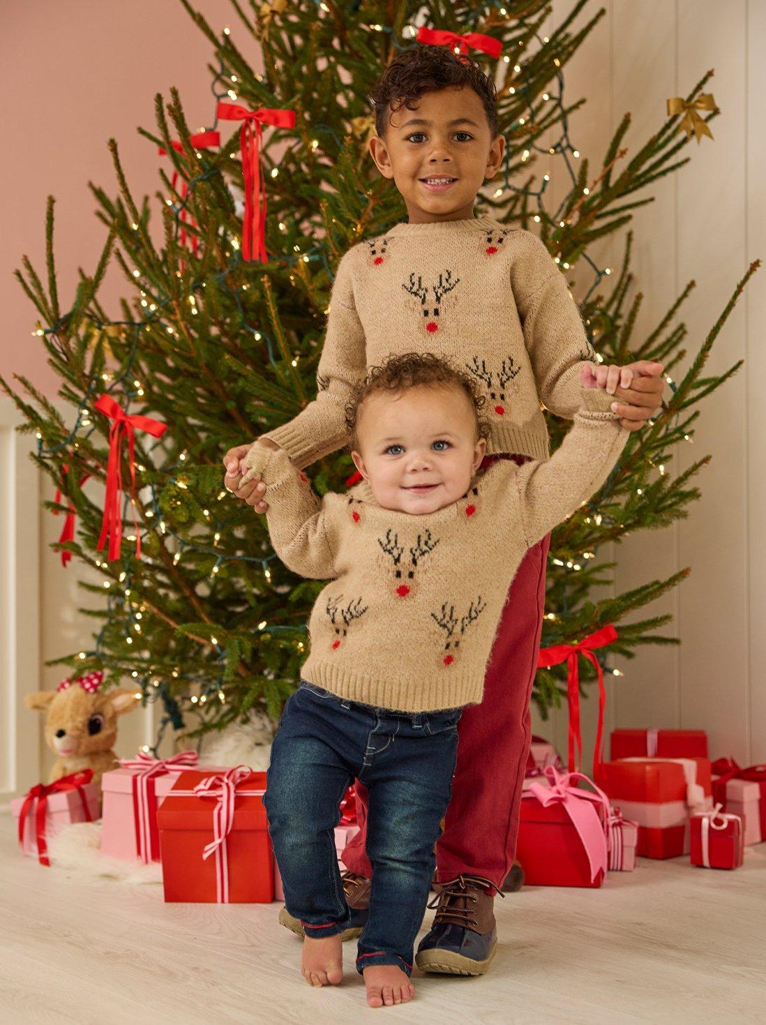 Two boys in tan matching reindeer sweaters.