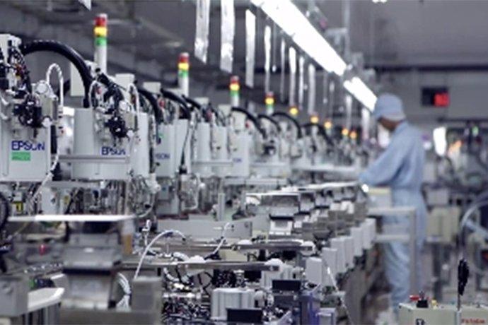 A row of machines with a person in a work jumpsuit standing in front of them seen in the distance