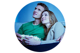 a man and woman sitting on a couch holding a bowl of popcorn