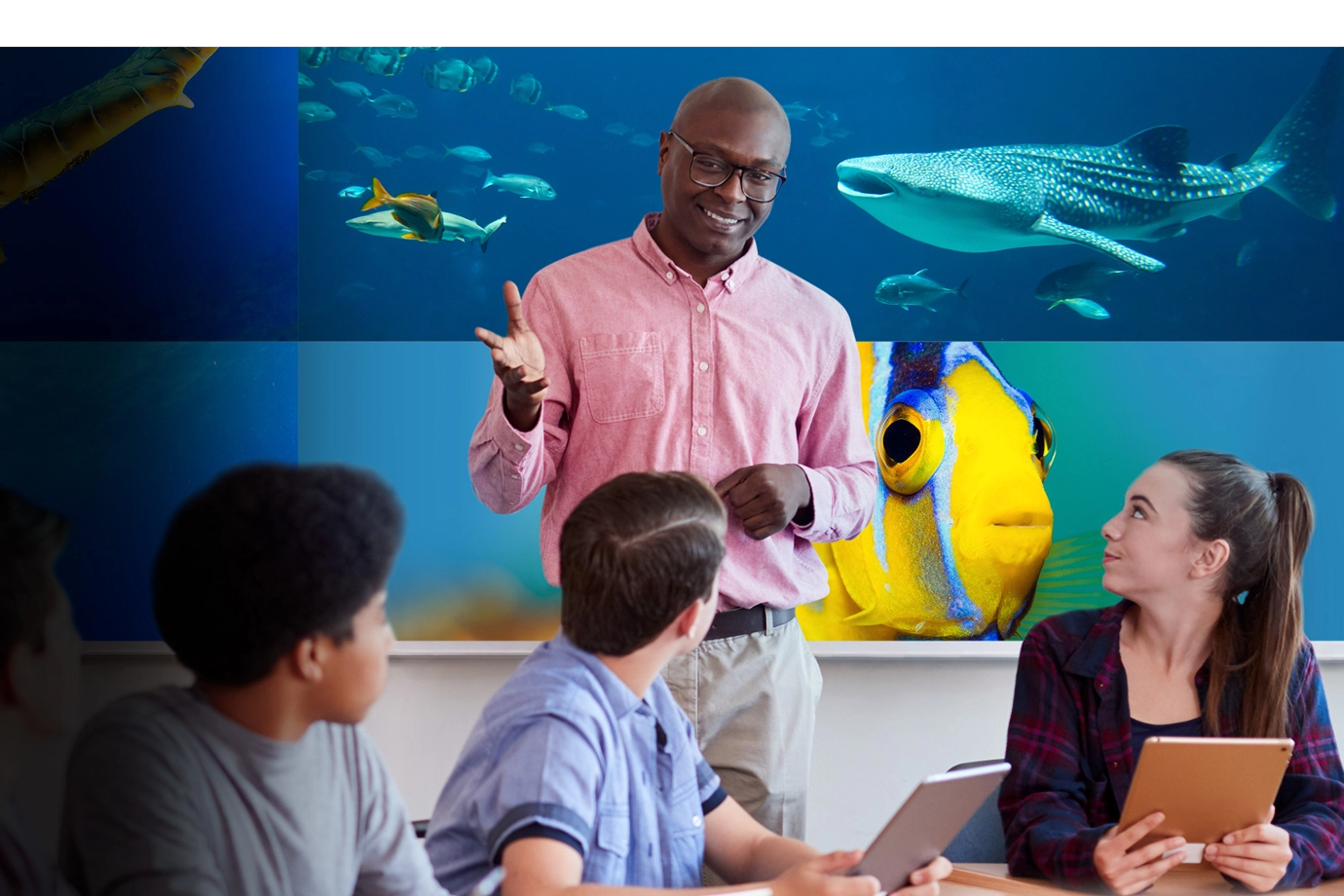 A teacher in a pink shirt talks to three attentive students.