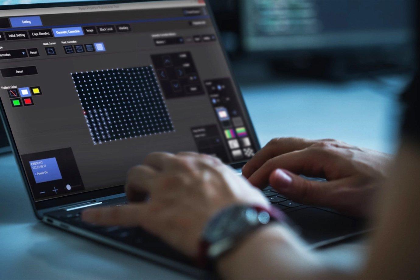 Hands on a laptop keyboard with a software interface displayed, showing grid patterns and colour controls.