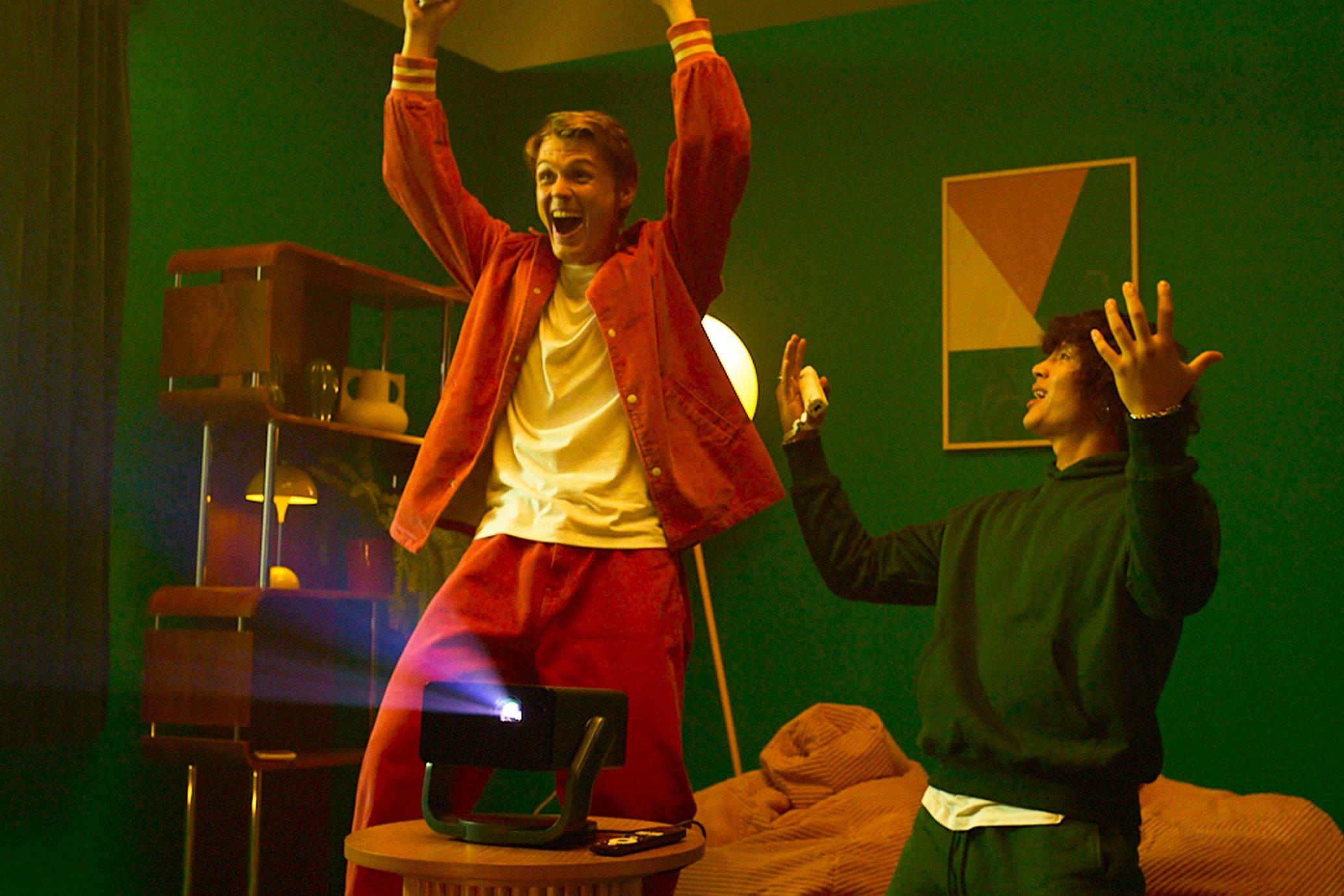 Two friends watching something on an Epson portable projector  at home - one is cheering
