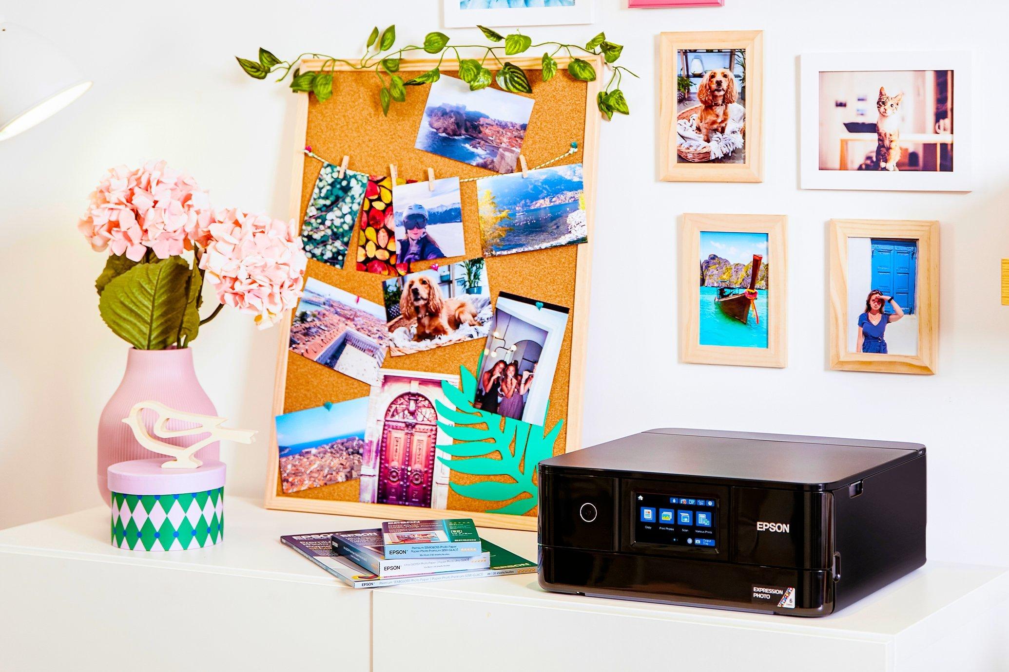 An Epson Expression printer on a desk with printed photos stuck on the board behind it