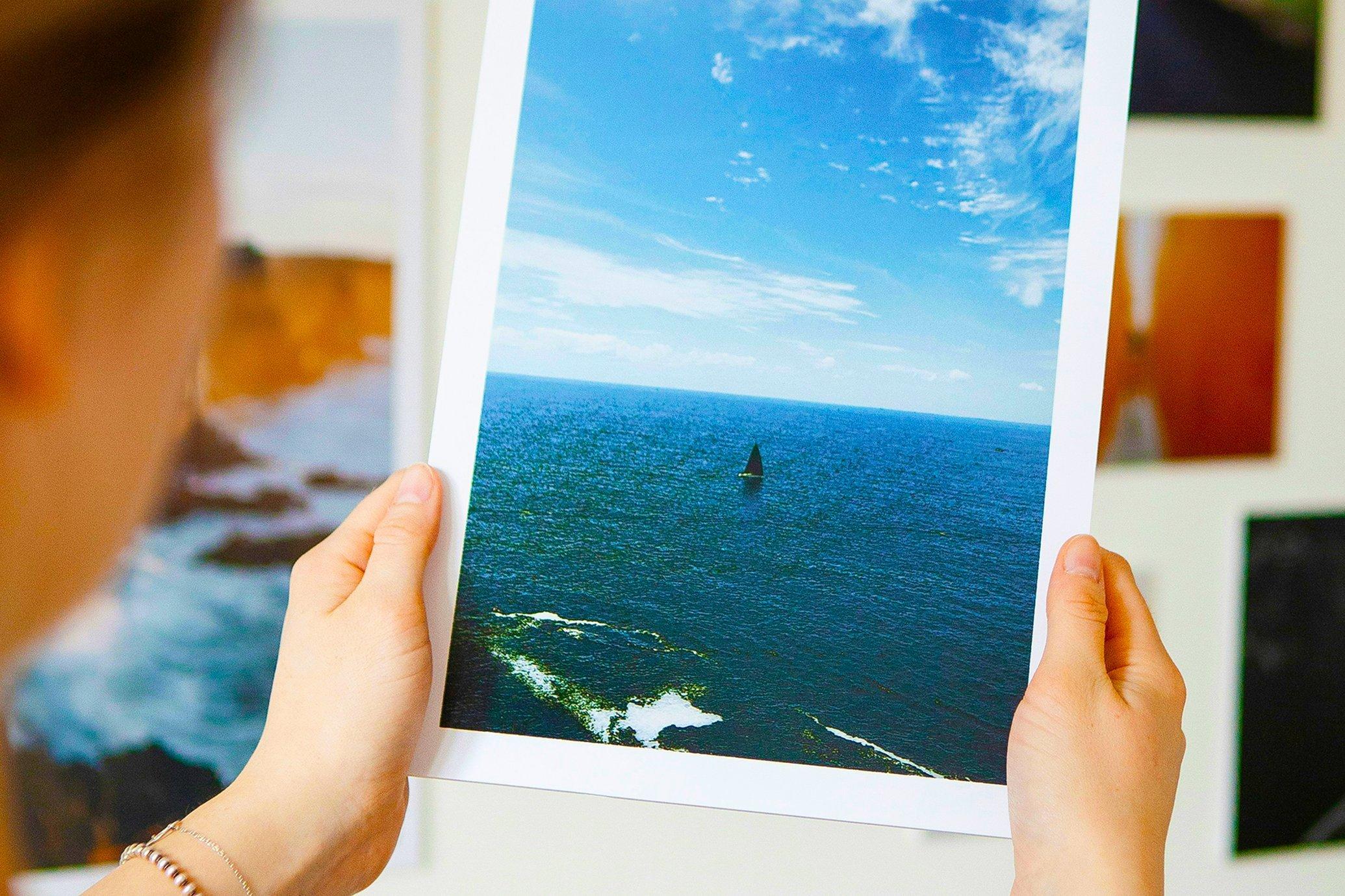 A woman looking at a vibrant photo print of the sea and sky
