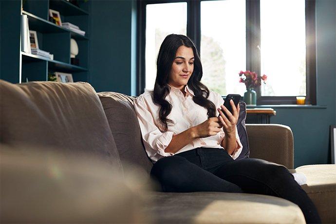 A woman sitting on a couch, looking at her smartphone.