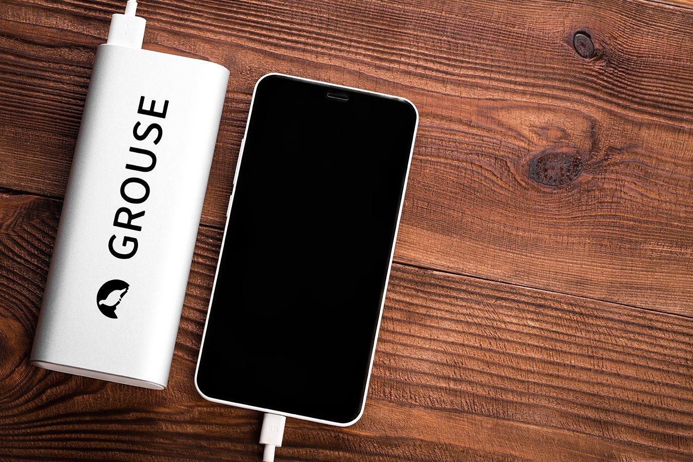 A black smartphone connected to a white power bank labeled "GROUSE" with a small logo.