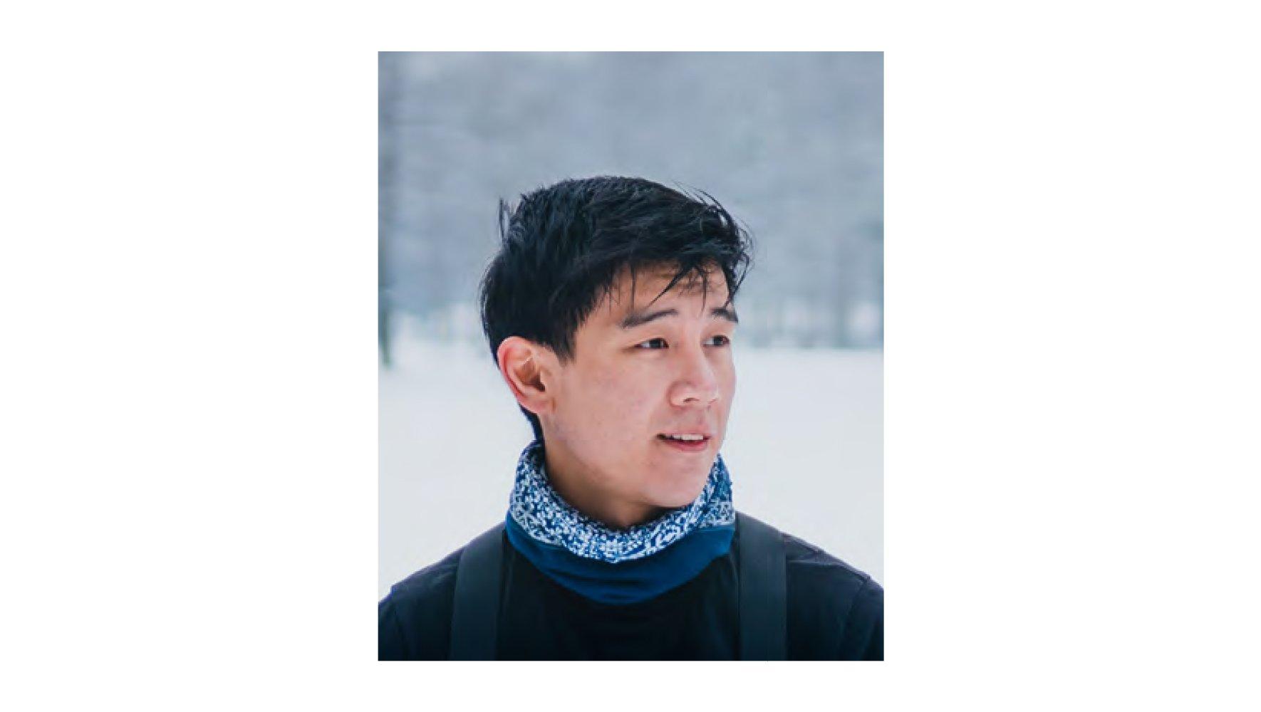 Photo of photographer Liam Man wearing winter clothes and a backpack against a winter scenery