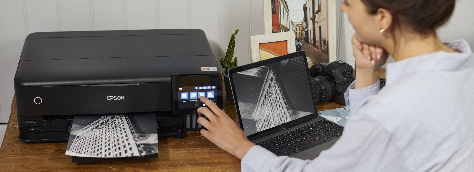 A person uses a laptop and an Epson printer to print a black-and-white photo of a building.