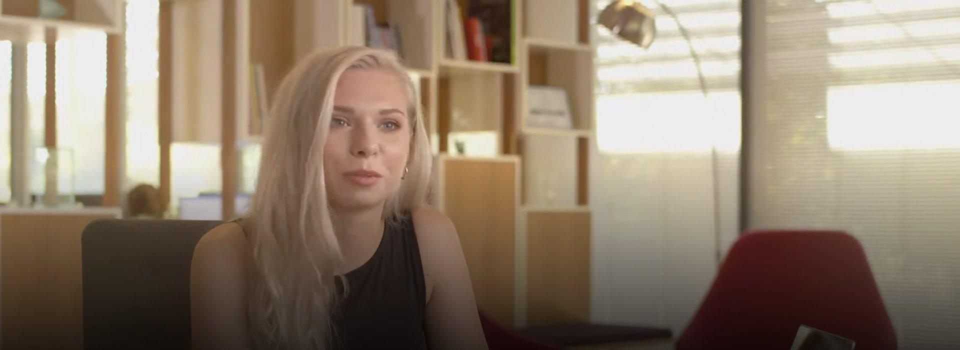 Talia, a blonde woman, sits at a desk in an open, shared space in a university.