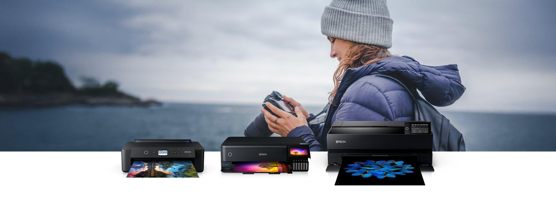 3 Epson printers are overlayed in front of a photo of a woman on the coast, looking at her DSLR camera.