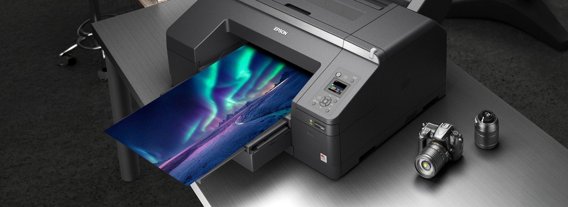An Epson printer printing a vibrant photo of the northern lights. A camera and lens sit on the table beside the printer.