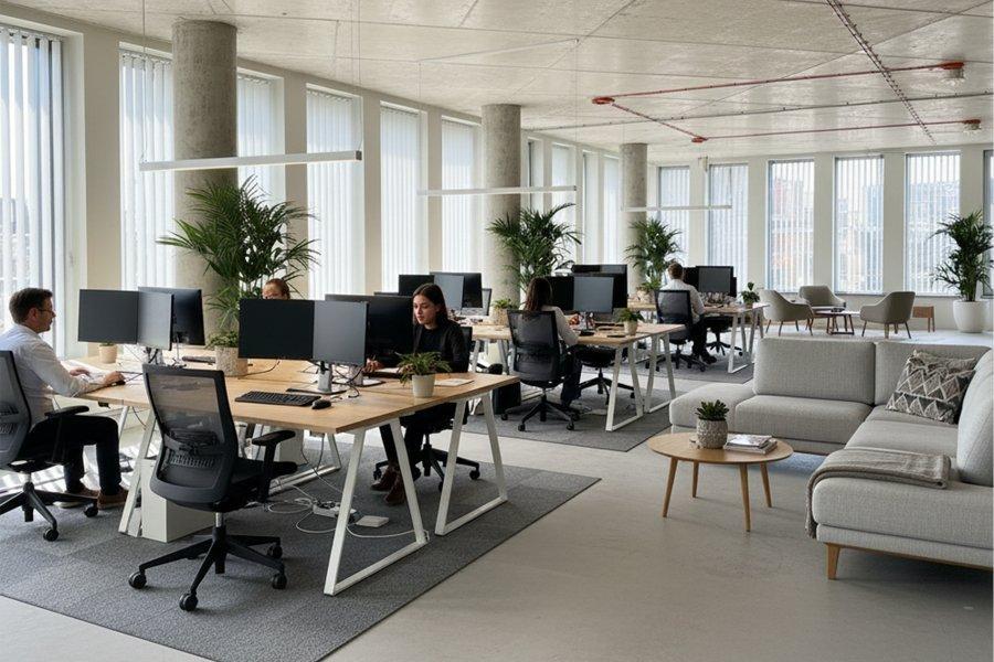 Moderns atvērta tipa birojs ar dažādiem darbiniekiem pie saviem galdiem, dažādām atpūtas zonām un podos augošiem augiem.