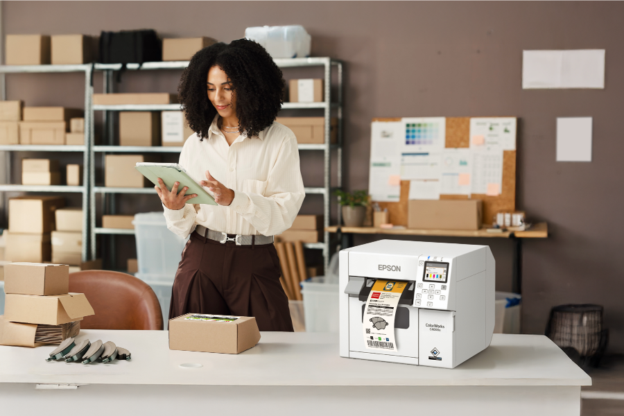 A woman using a tablet, with an Epson printer printing off various labels in the foreground.
