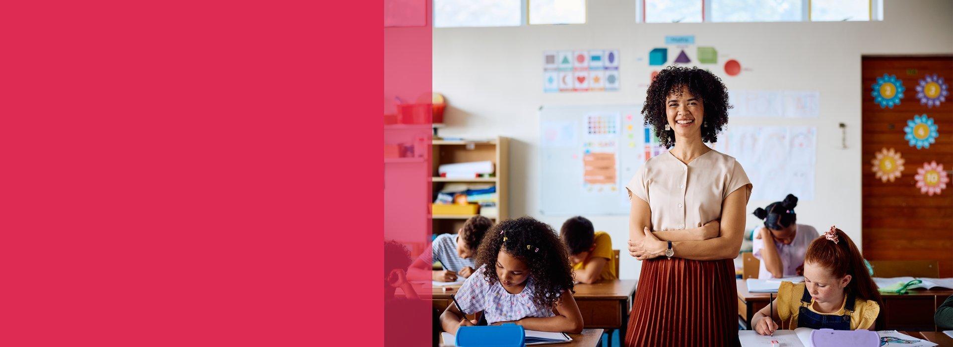 Teacher standing in a classroom while students are doing their work.