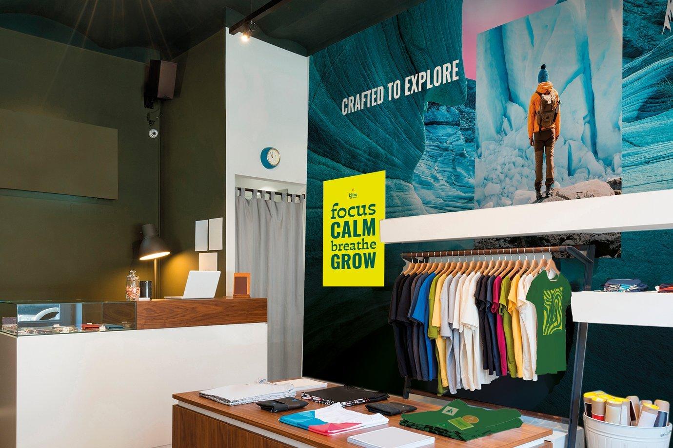 Clothing store interior with colorful shirts on racks, a modern checkout counter, and a large mural saying "Crafted to Explore." Bright and inviting.