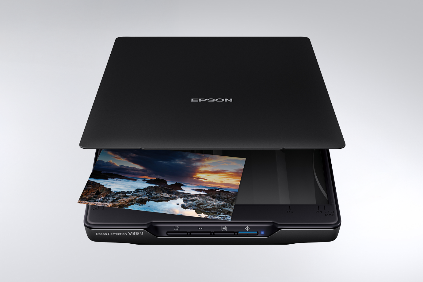 An Epson scanner with a black lid partially open, scanning a vibrant photo of a rocky coastline at sunset. The image conveys a professional and calm tone.