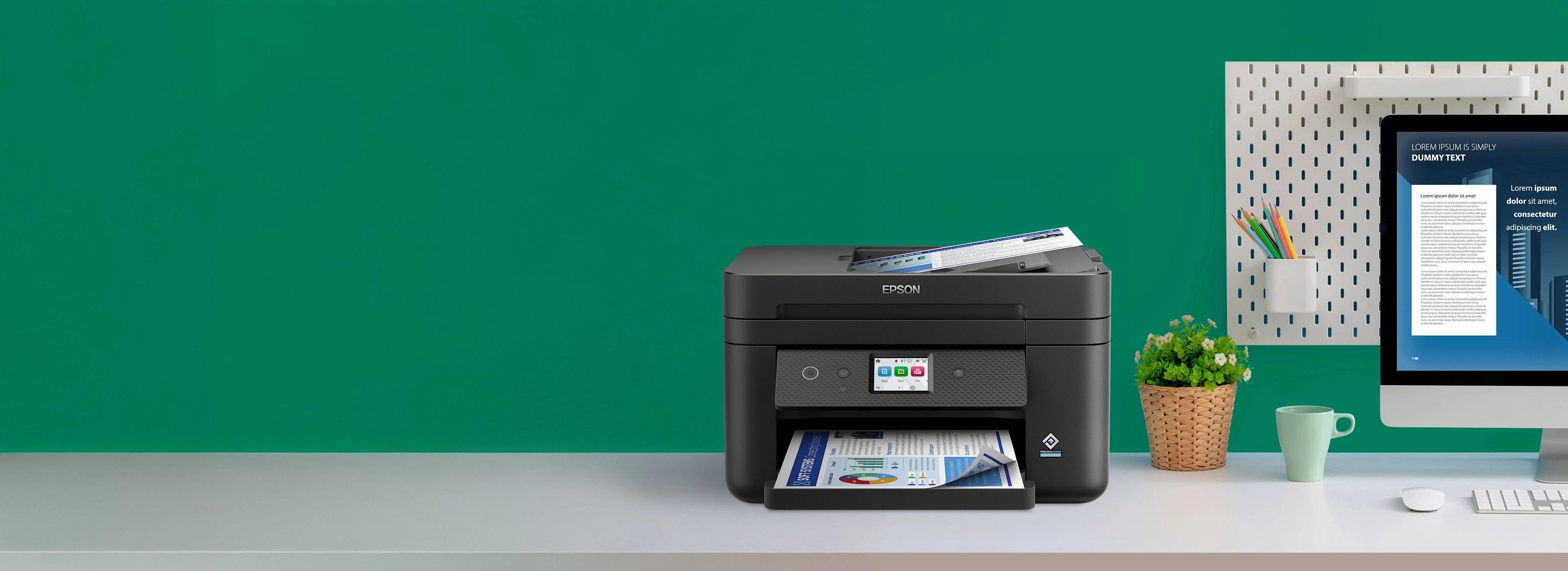 A black Epson printer on a desk with colorful documents, next to a computer monitor displaying text. A green wall and potted plant add vibrancy.