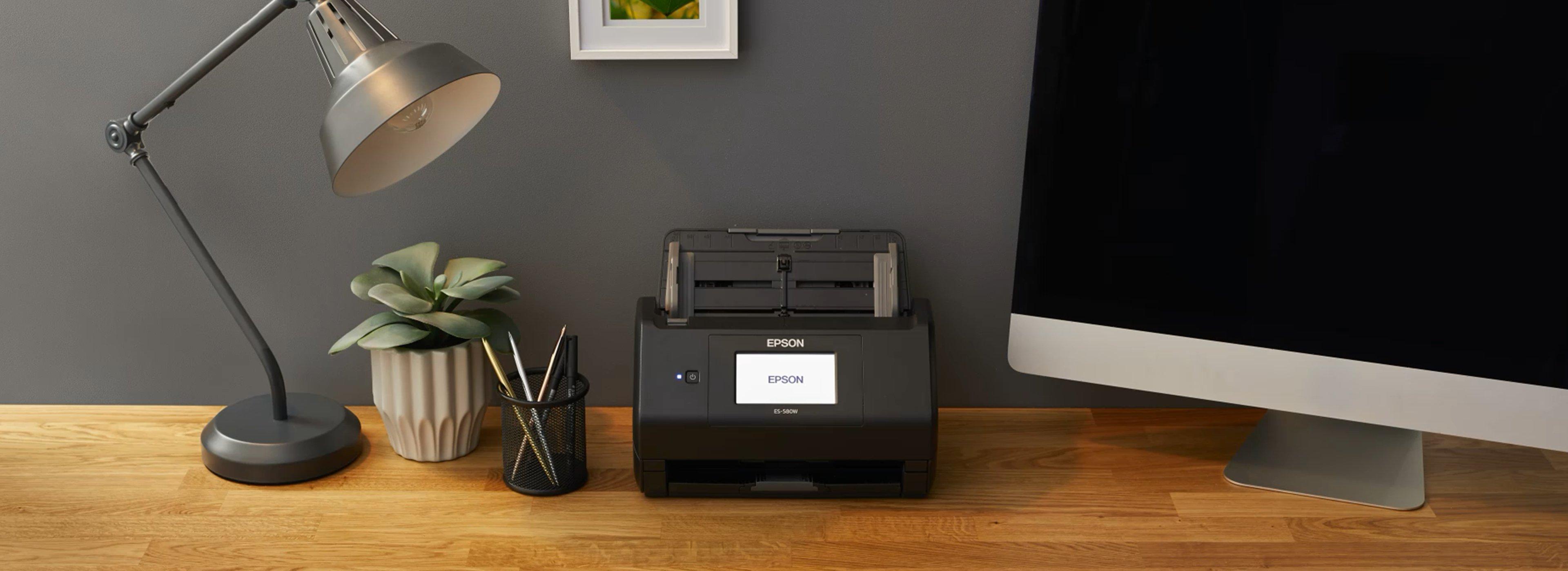 A modern desk setup with a sleek Epson printer beside a large computer monitor.
