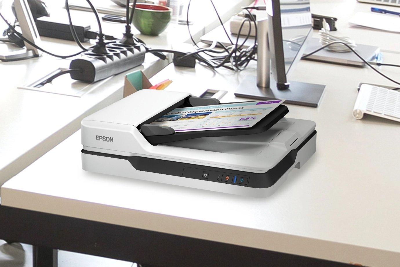 A sleek, modern scanner sits on an office desk, surrounded by computers, papers, and cables.