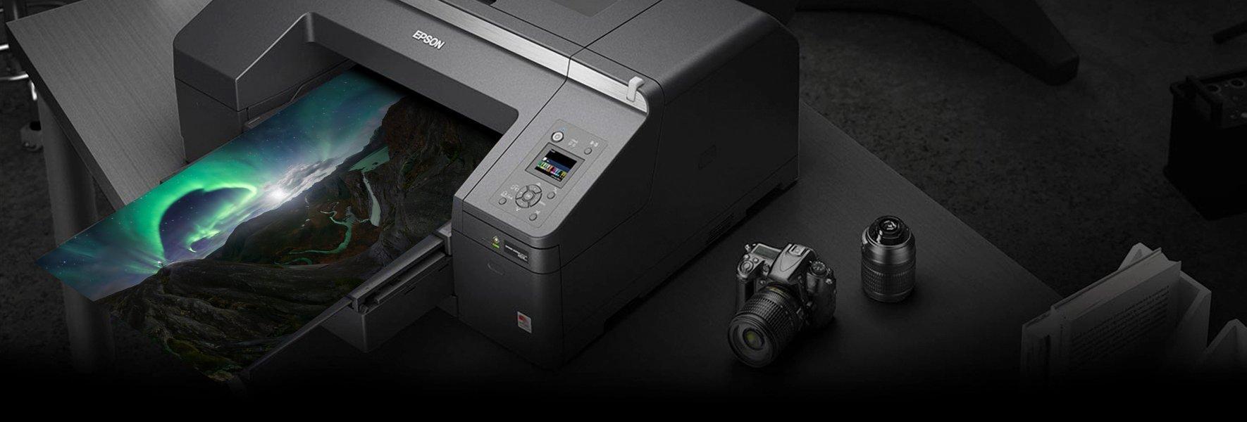 An Epson printer printing a photo of a vibrant green aurora borealis in the night sky over a rugged landscape with winding rivers, rocky terrain, and distant lakes under a star-filled sky.