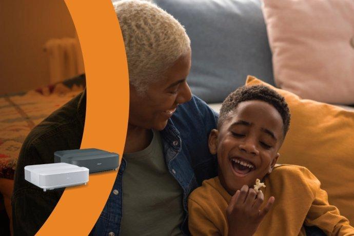 A father and son sat together at home smiling. The son is eating popcorn. Two Epson Lifestudio projectors are overlayed atop the image.