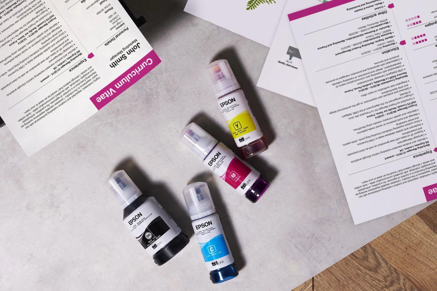Four Epson ink bottles in black, cyan, magenta, and yellow are on a gray surface near a resume labeled "Curriculum Vitae," creating a vibrant, professional tone.