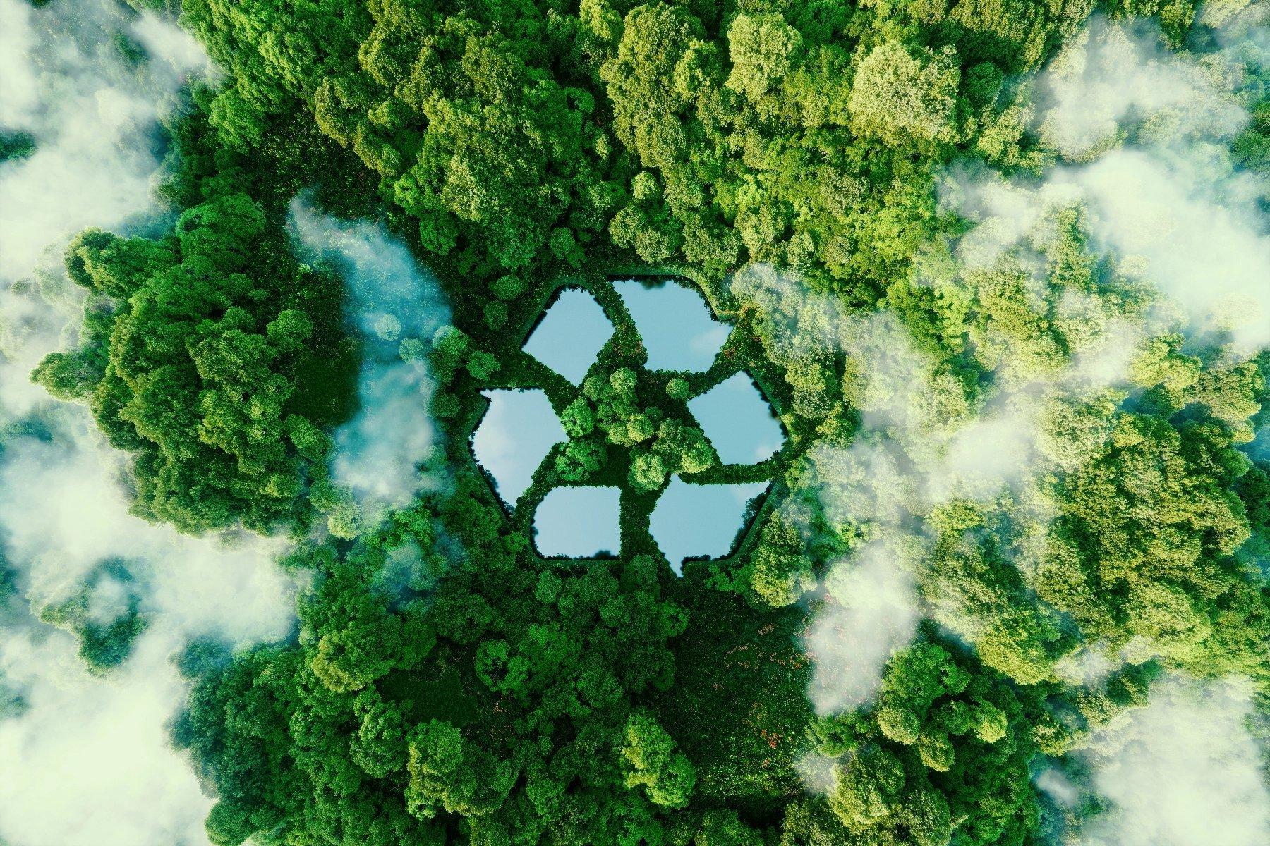 Aerial view of a lush green forest with a large, geometric recycling symbol formed by ponds in the center, surrounded by mist and trees.
