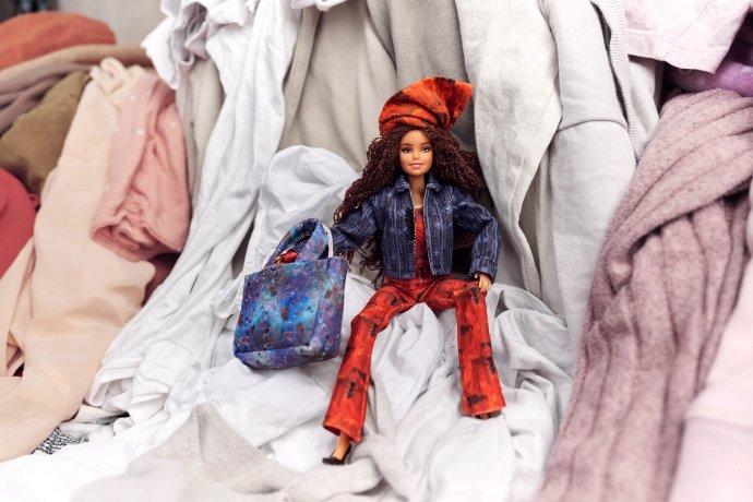 Boneca da moda repousando sobre uma pilha de roupas.