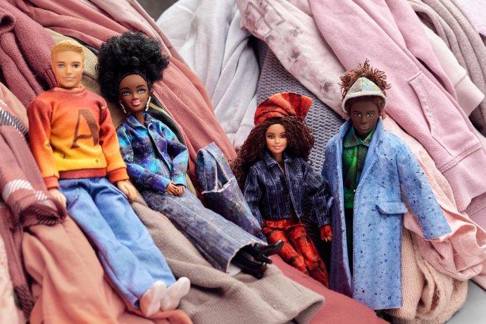 Quatro bonecas da moda repousando sobre uma pilha de roupas.