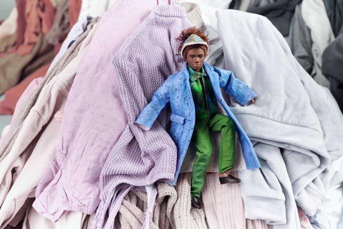 Boneca elegante repousando sobre uma pilha de roupas.