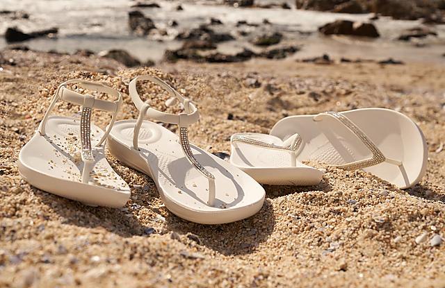 Fitflop Iqushion Flipflops in white with shimmer details on a beach.