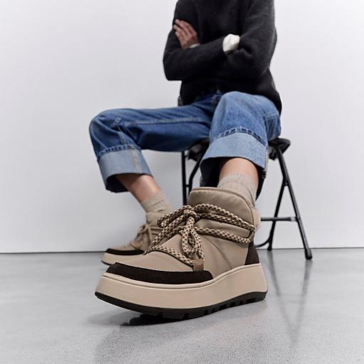 Persona sentada que lleva zapatillas deportivas altas color beige con cordones gruesos y pantalones vaqueros remangados.