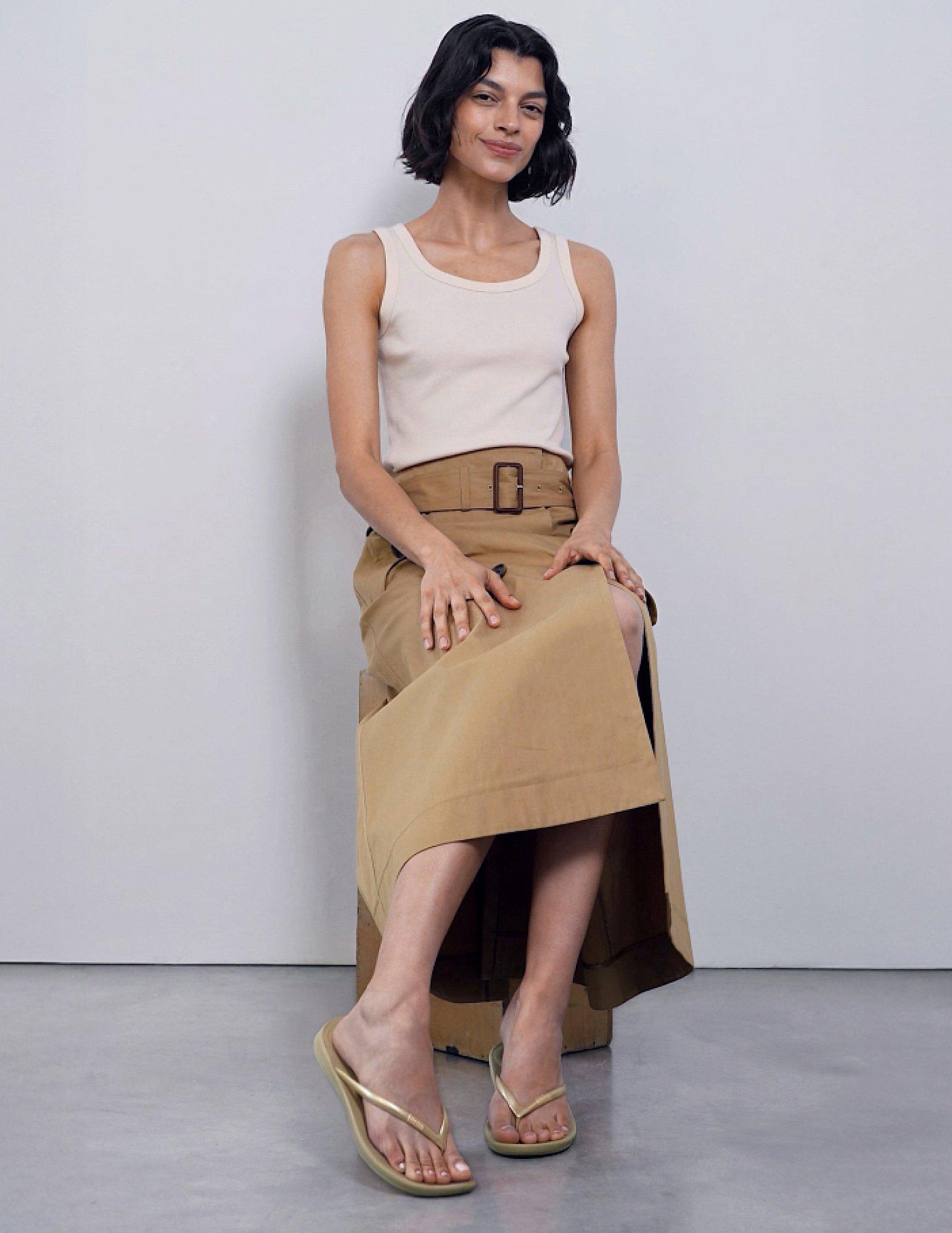 Person seated wearing khaki flip-flops against a plain background