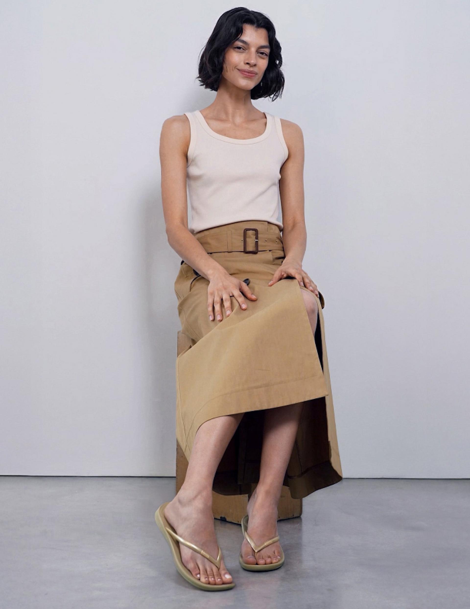 Person seated wearing khaki flip-flops against a plain background